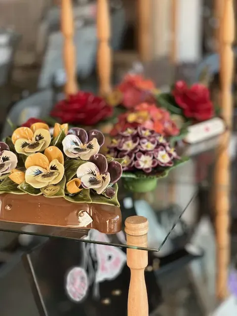 Compositions de fleurs en céramique décoratives exposées sur des étagères en verre dans une vitrine.