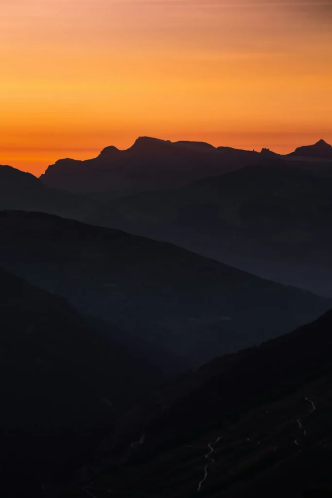 Silhouette de montagnes au crépuscule sur fond de ciel orangé.