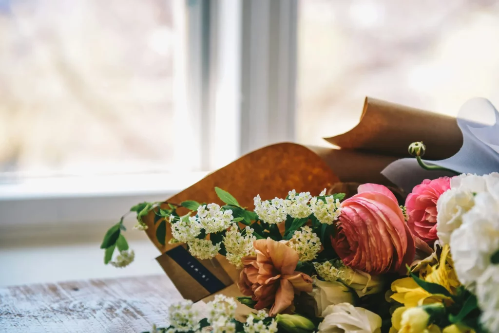 Bouquet de fleurs fraîches emballé dans du papier kraft posé sur une table près d'une fenêtre